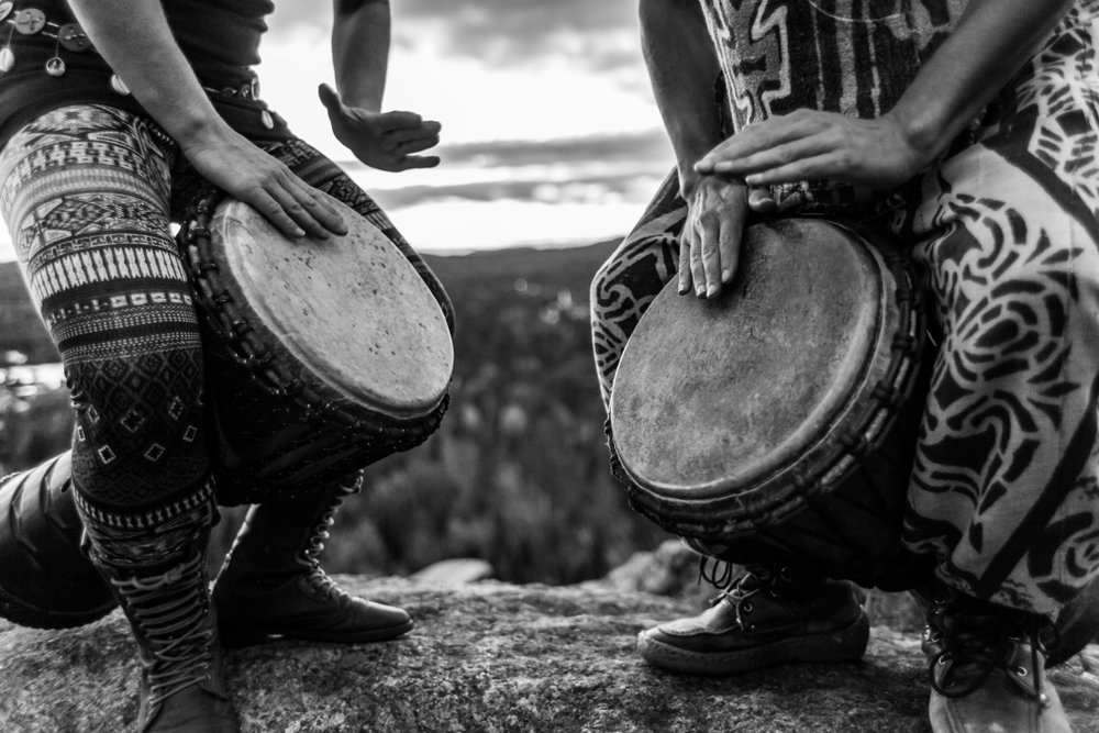 2 people standing & drumming on djembes
